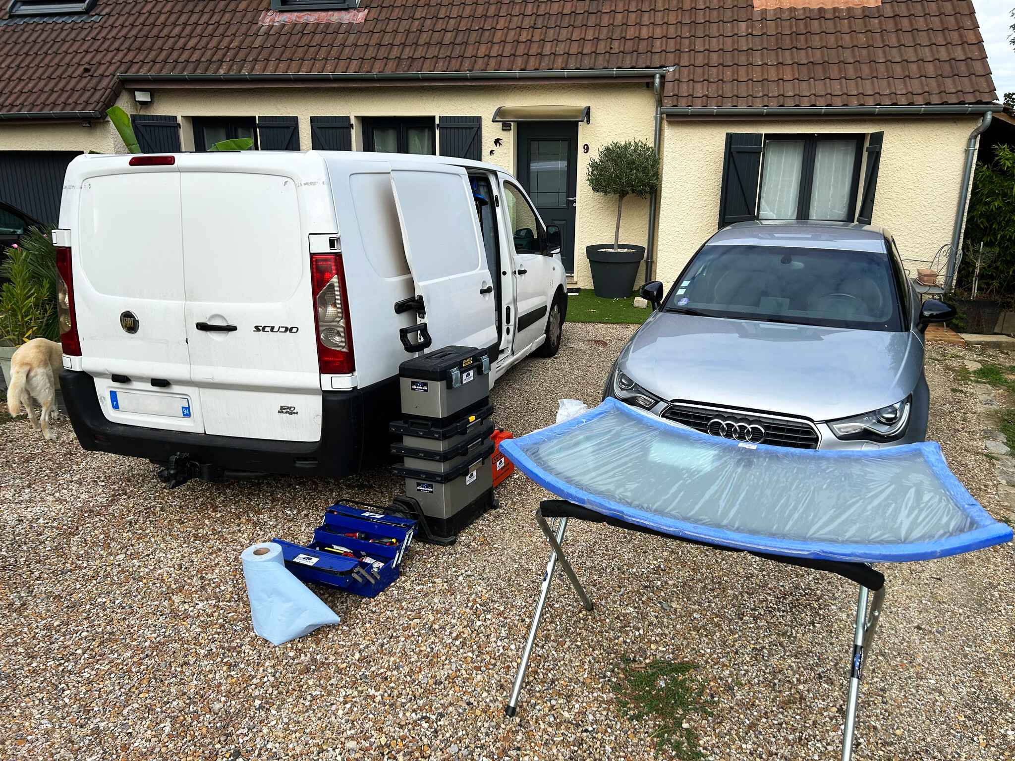 La camionnette de Luso Glass Auto garée devant une maison, avec le pare-brise neuf sur son support à côté de la voiture du client