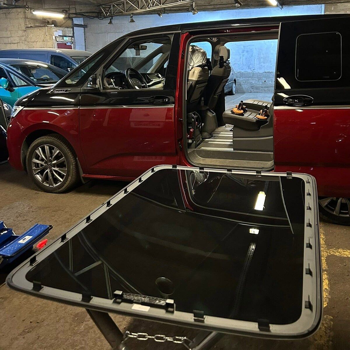 Vitre de toit panoramique sur son support, devant un van Volkswagen portière ouverte